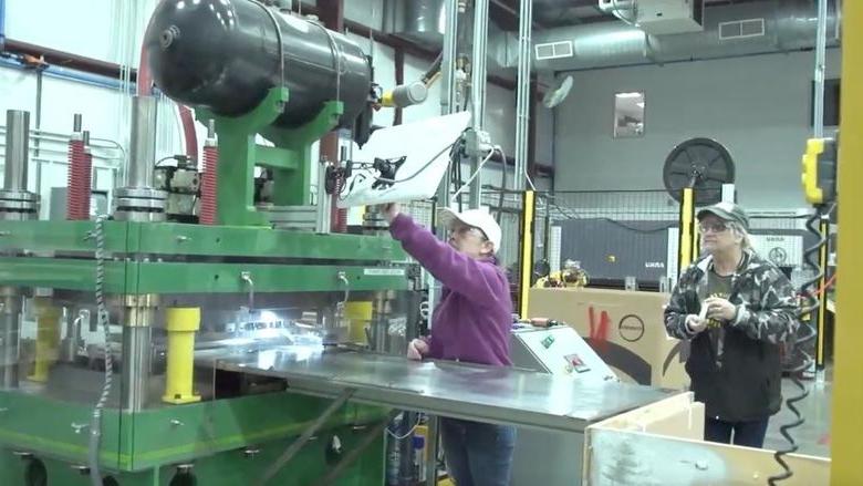 Two people in baseball caps and safety glasses work in a manufacturing plant 