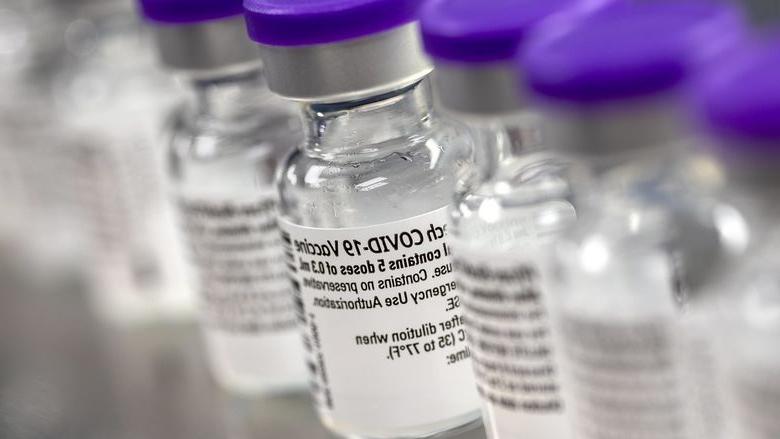 A row of vials show labels indicating they contain the COVID-19 vaccine.