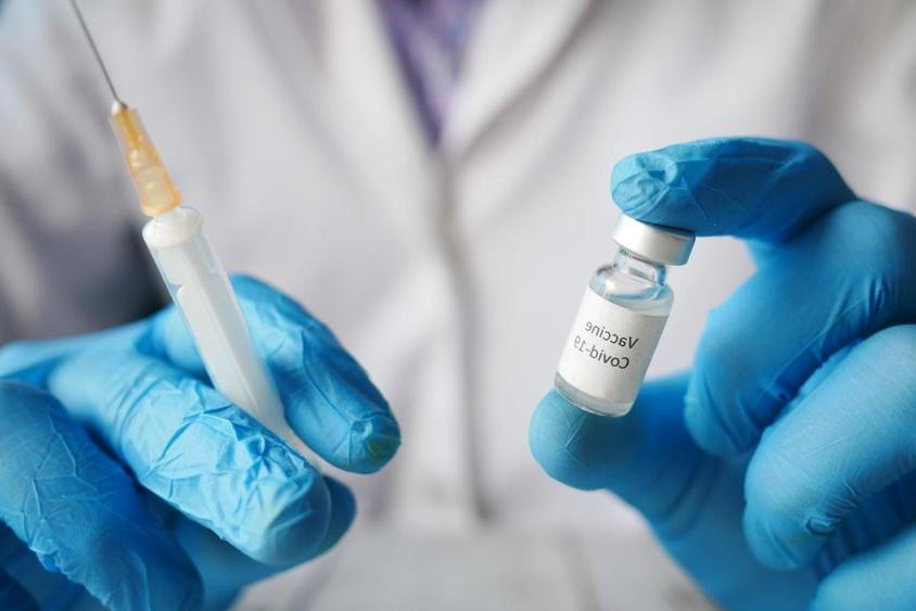 A person wearing blue gloves holding a COVID-19 vaccine vial and a syringe